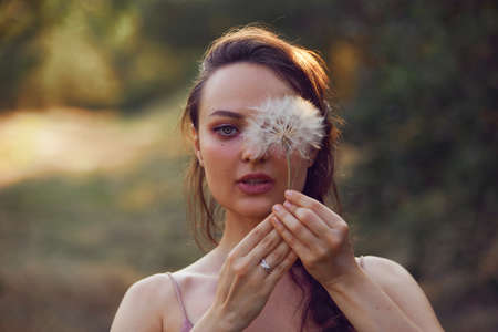 Beautiful woman hold near face dandelion in the park. Free space for textの写真素材