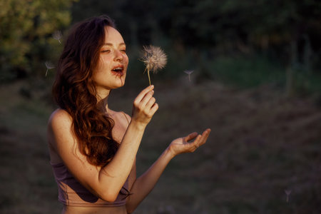 Beautiful happy woman blowing big dandelion. Outdoors, enjoy nature. Healthy smiling woman on summer lawn. Allergy free concept. Gorgeous slim caucasian, free space for textの写真素材