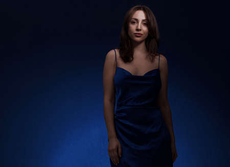 Young and cute brunette woman in blu dress posing on dark blue background free space for textの写真素材