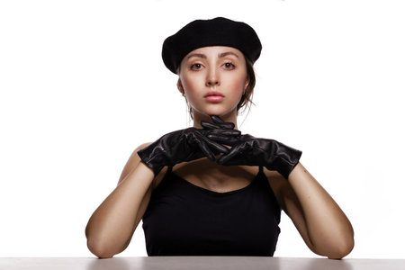 Strategy and solution concept. Portrait of gorgeous young fashion model in black beret and leather gloves leaning on the table on white background.の写真素材