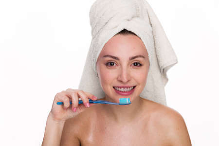 Cute and excited beautiful woman holds toothbrush and wearing towel on her head. Female has cleen skin shows white teeth, poses with naked body isolated over white backgroundの写真素材