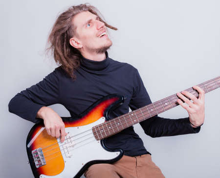Funny dreadlocked man sitting and play on bass guitar. Enjoys and love music over gray background copy spaceの写真素材