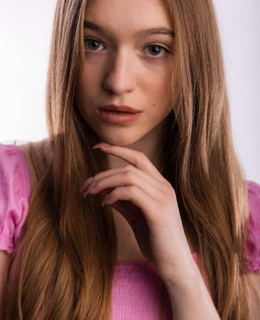 Beautiful natural young woman face with blond long hair posing and smiling at camera isolated on white. Care and health concept of the head and hairの写真素材