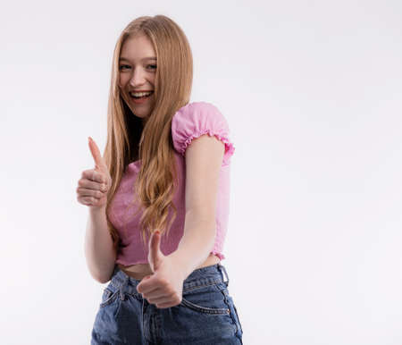 Happy smiling blonde woman or female student or customer with broad smile showing thumbs up with both hands looking at the camera with happy expression over white backgroundの写真素材