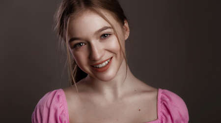Beautiful woman smiling. Pretty joyfully female with fair hair, dressed casually, looking with satisfaction at camera, being happy. Studio shot of good-looking beautiful woman on dark studio wall.の写真素材