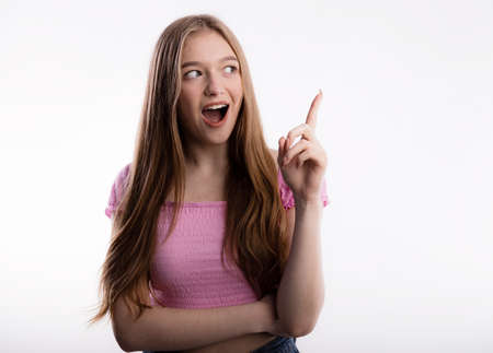 Young beautiful woman having an idea. Expressive wide open mouth and pointing her finger up over white backgroundの写真素材