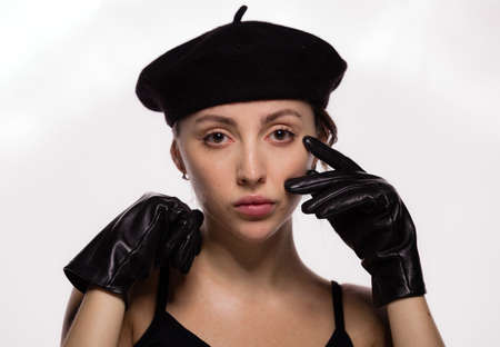 Portrait of gorgeous young fashion model in black beret and leather gloves posing on white...