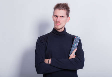 Man holding TV remote control. Dreadlocks man in dark gray turtleneck isolated on gray background copy space. Studio shot shocking TV contentの写真素材