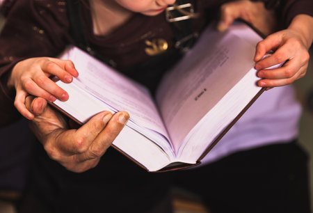 Grandfather and granddaughter read a big book at home library. Close up old hands and kid hands together holding a book focus on hands. Home comfort, hobby education and experienceの写真素材