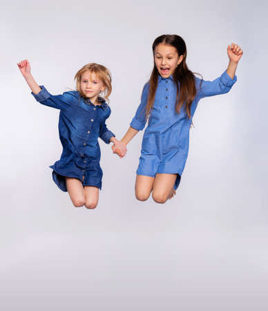 Full size portrait of two excited cute children girls enjoy jumping open mouth isolated on gray background. Loving sisters or friends jumping up playing and having funの写真素材