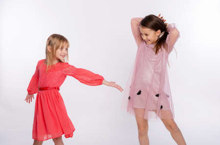 Playful kids, funtime concept. Portrait of cute two girls 6-8 years old wearing pink dress and dancing isolated on white background. Mother's Day, love family, parenthood childhood conceptの写真素材
