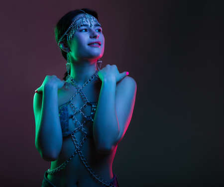 Portrait of a woman wearing fashionable luxury jewelry chains, in an oriental suit and diadem. Scheherazade's fairy tale in colorful bright neon blue and purple lights.の写真素材