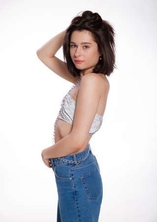 A beautiful woman posing in a jewelry bra with chains and blue jeans isolated on white background. Mockup for party or dance concept with space for textの写真素材
