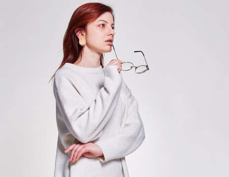 Redhead young woman hold in hand eyeglasses near face standing on isolated white backgroung, copy space. learning and teaching concept or make announcement advertisementの写真素材