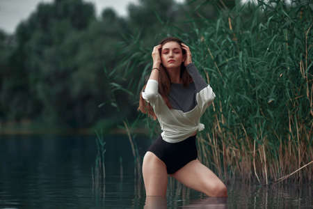 Attractive young brunette in a sweater and and black pantians posing on the reeds beach. Beach fashion, seductive woman resting near the waterの写真素材
