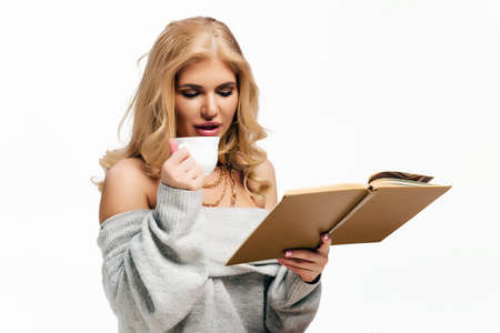 Portrait of cozy woman in knitted winter white warm sweater drinks a cup of hot coffee or tea during...