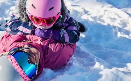 Mother and daughter in ski equipment together lying in snow enjoying wintertime are having fun at ski resort. Happy family playing in snowの写真素材