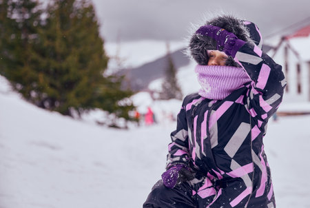 Portrait of little smiling girl enjoying winter vacation. Child in knitted hat and face cover collar...