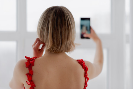 Girl in red dress makes selfie on smartphoneの写真素材