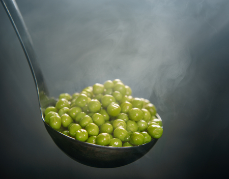 Boiled peas in a scoop on a dark background with smoke