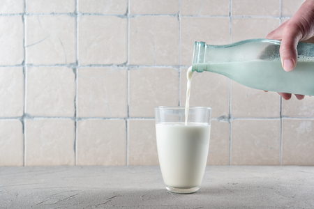 Pouring milk on the kitchen background with ceramic tilesの写真素材