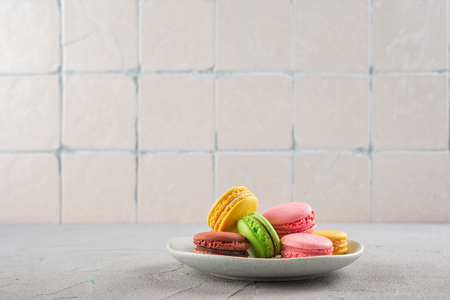 Multicolored Macaroni cookies on a plate on the kitchen background with ceramic tilesの写真素材