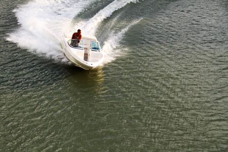 A man in a trench manages a motor boat on the riverの写真素材