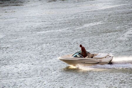 A man in a trench manages a motor boat on the riverの写真素材