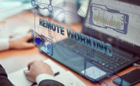 Hands of a businessman using a laptop with smart phone and futuristic holographic screen in currency rate charts. Remote home work concept. Background of a remote office.の写真素材