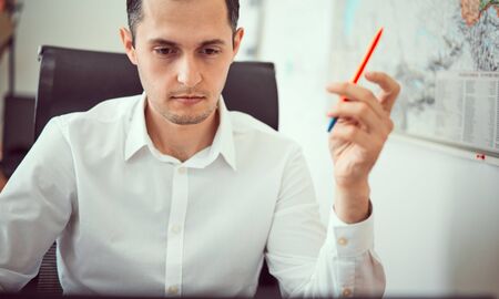Closeup portrait of a young male, happy, cheerful, handsome businessman sitting at a computer desk in a modern office using a laptop computer for work.の写真素材