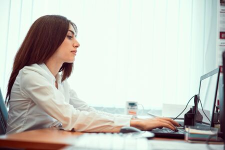 Closeup portrait of a young happy, happy, cheerful, beautiful business girl sitting at a computer table in a modern office using a laptop computer to work.の写真素材