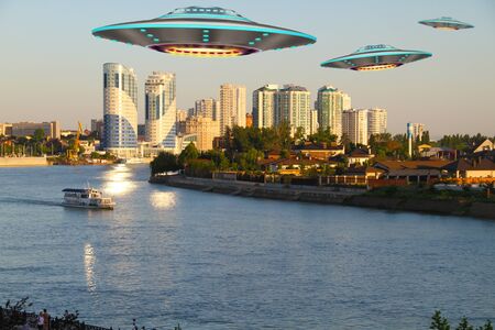 A metal and silver UFO invasion of planet Earth, a group of spaceships fly in the sky above the city and emit yellow rays to the earth. 3D renderingの写真素材