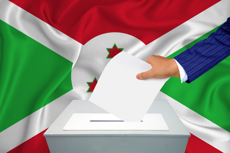 Elections in the country - voting at the ballot box. A man's hand puts his vote into the ballot box. Flag Burundi on background.の写真素材