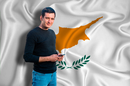 Cyprus flag on the background of the texture. The young man smiles and holds a smartphone in his hand. The concept of design solutions.の写真素材