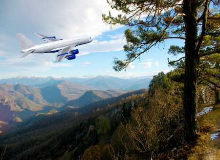 Commercial white plane airliner flying over dramatic clouds and mountains. Travel concept.の写真素材