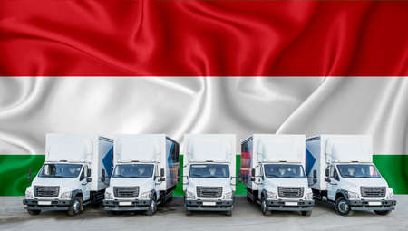 Hungary flag in the background. Five new white trucks are parked in the parking lot. Truck, transport, freight transport. Freight and logistics conceptの写真素材