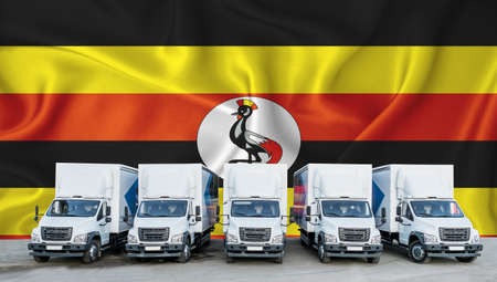 Uganda flag in the background. Five new white trucks are parked in the parking lot. Truck, transport, freight transport. Freight and logistics conceptの写真素材