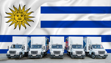 Uruguay flag in the background. Five new white trucks are parked in the parking lot. Truck, transport, freight transport. Freight and logistics conceptの写真素材