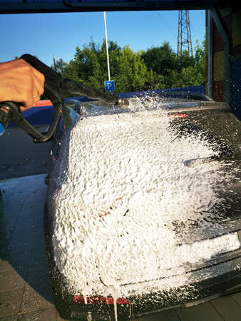 A young man at a car wash washes the car under high pressure. Selective focus.の写真素材
