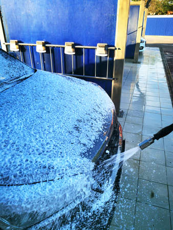 A young man at a car wash washes the car under high pressure. Selective focus.の写真素材