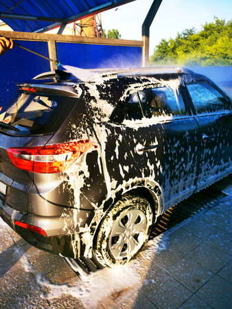 A young man at a car wash washes the car under high pressure. Selective focus.の写真素材