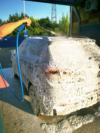 A young man at a car wash washes the car under high pressure. Selective focus.の写真素材