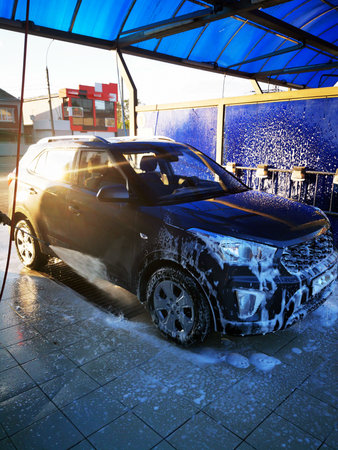 A young man at a car wash washes the car under high pressure. Selective focus.の写真素材