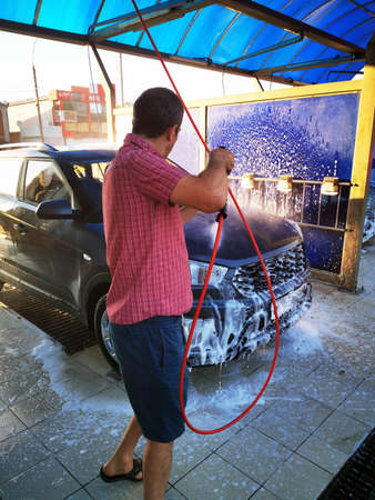 A young man at a car wash washes the car under high pressure. Selective focus.の写真素材