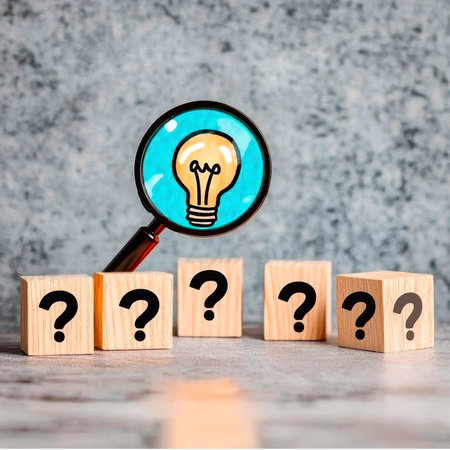 Concept illustration of a glowing light bulb under a magnifying glass among cubes with question marks symbolizes thinking and ideasの素材
