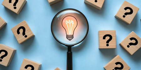Concept illustration of a glowing light bulb under a magnifying glass among cubes with question marks symbolizes thinking and ideasの素材