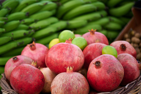 Ripe red pomegranates in a basket against a background of ripe bananasの写真素材