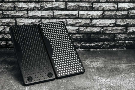 Black Sadhu wooden boards with nails for yoga on gray background and dark brick wall.