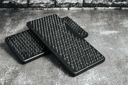 Black Sadhu wooden boards with nails for yoga on gray background and dark brick wall.