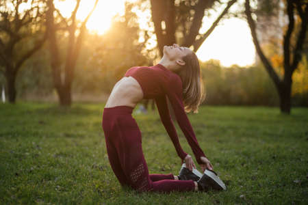 Young woman in red sportswear doing yoga pose on the sunset in the autumn park. Balance, fitness,...